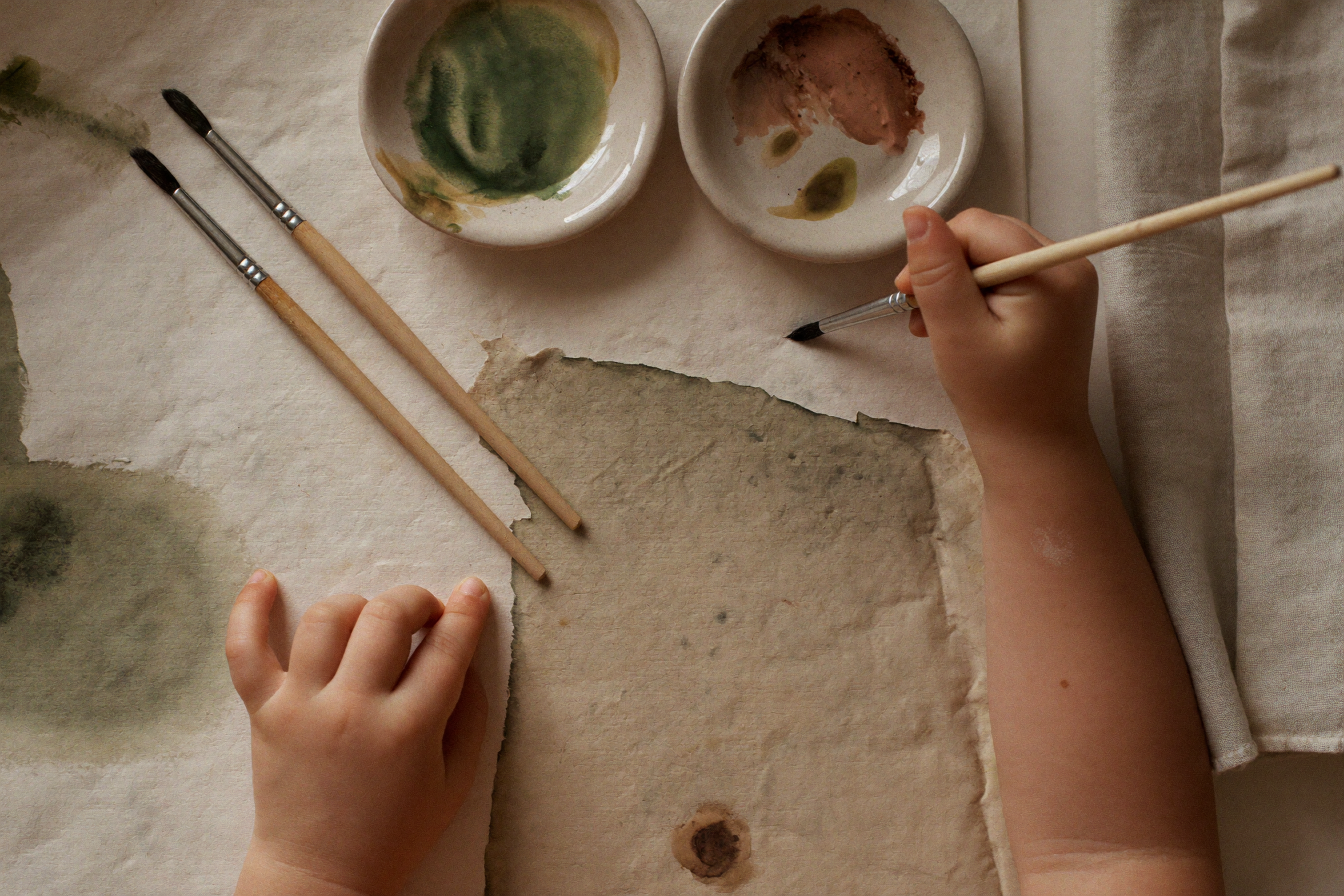 Small hands painting with earth-pigment watercolours on handmade paper.