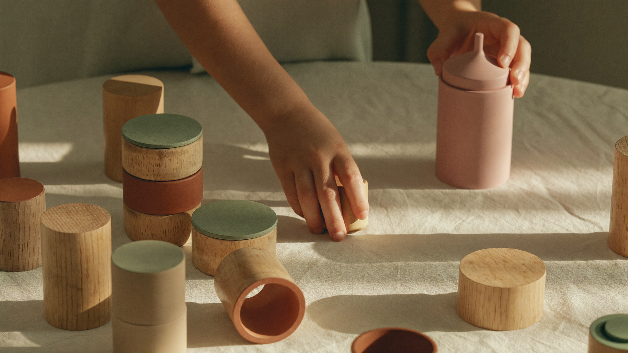 Small hands arranging wooden Montessori cylinder blocks on a cream linen surface in soft morning light.