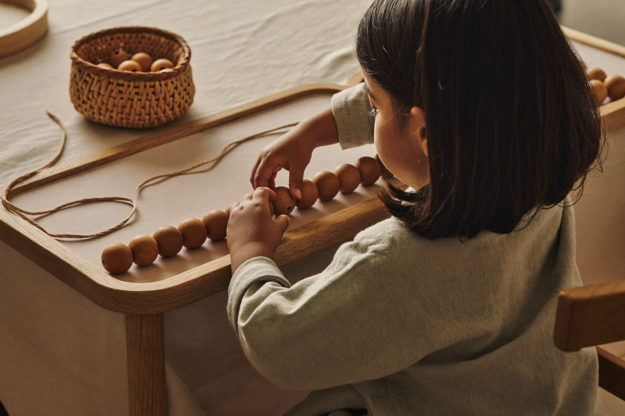 A young child carefully threading wooden beads on a Montessori bead frame at a small oak table, soft window light.